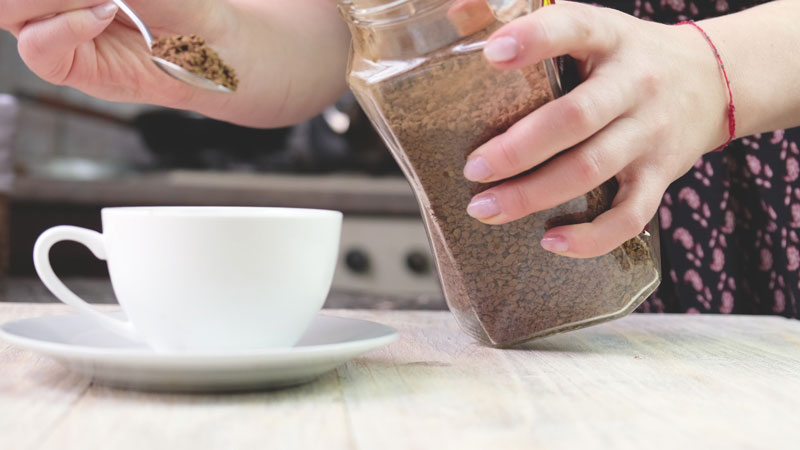 Instant coffee granules being added to a cup of hot water